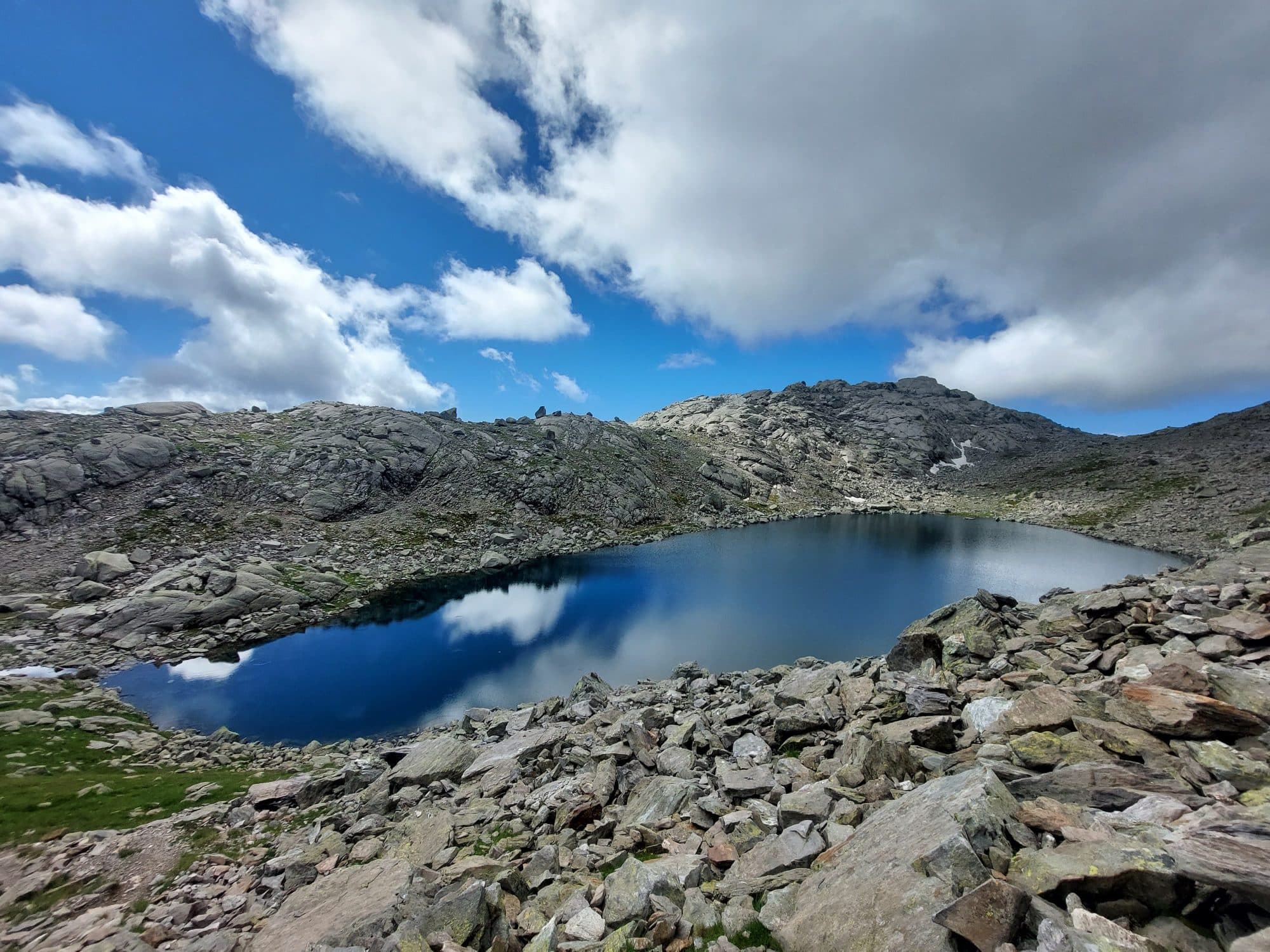 Stiller Bergsee zwischen Felsen unter Sommerwolken