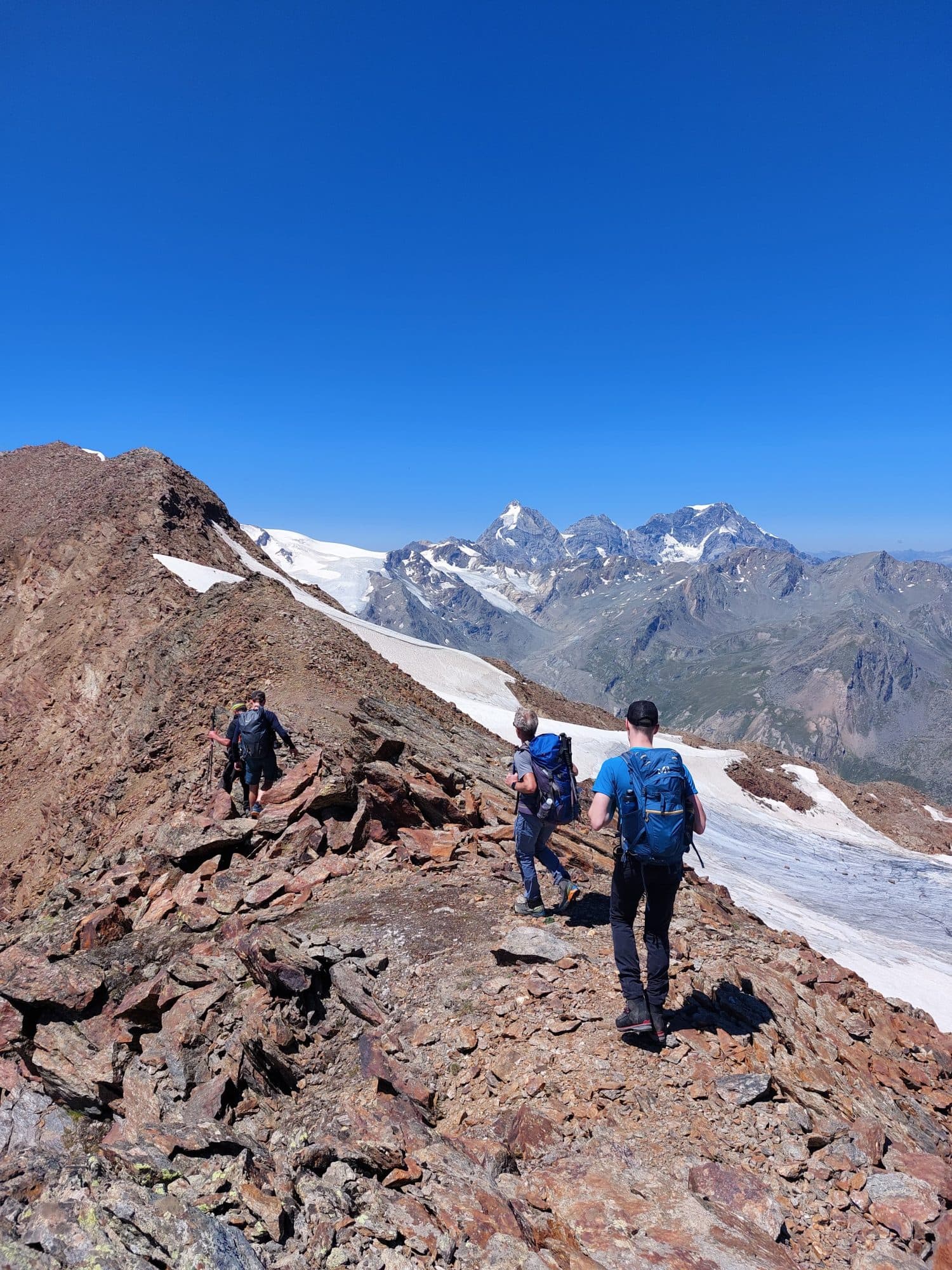 Kleine Wandergruppe auf einem Grat neben Schneefeldern