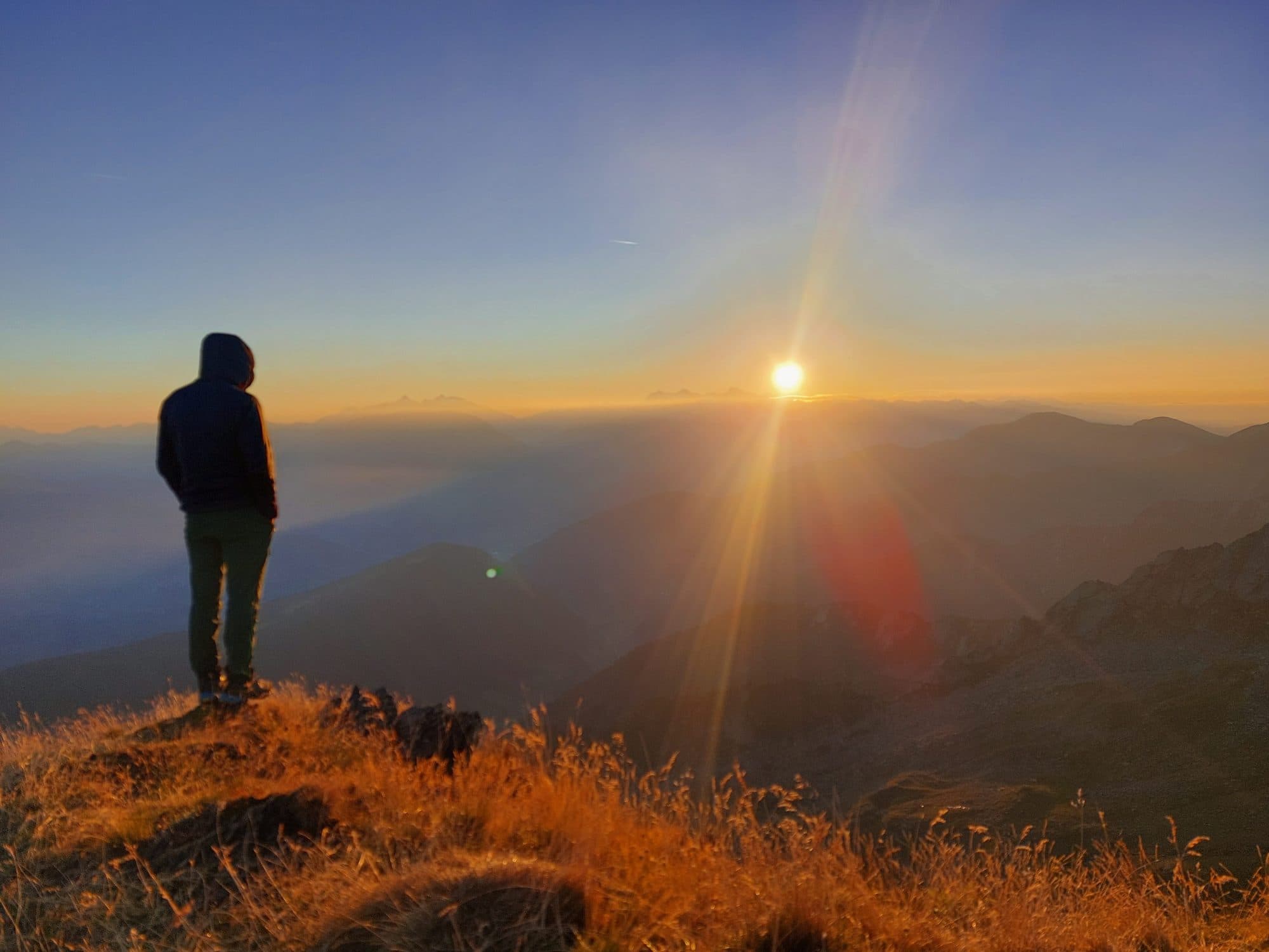 Wanderer blickt bei Sonnenaufgang über die Berge